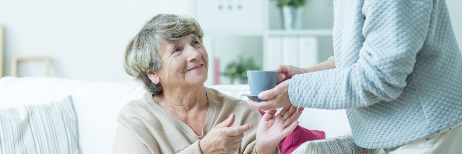care giver handing cup of tea to elderly woman 